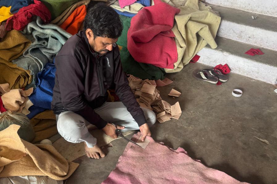 An artisan cutting pink wool felt, surrounded by coloured felt offcuts